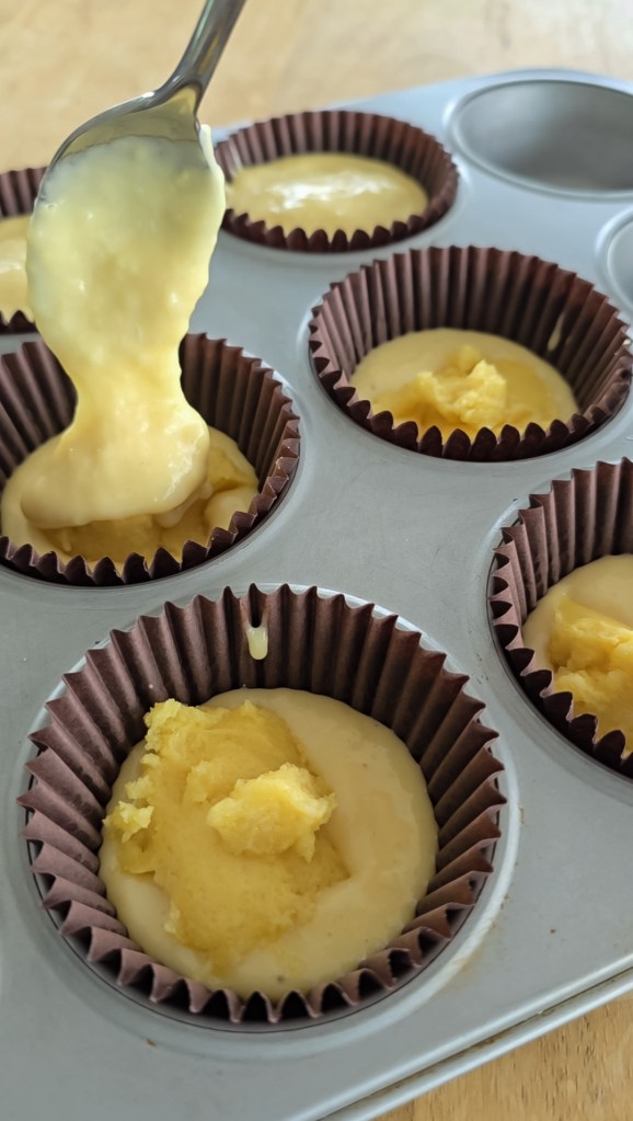 Muffin batter being put in muffin liner over frangipane filling