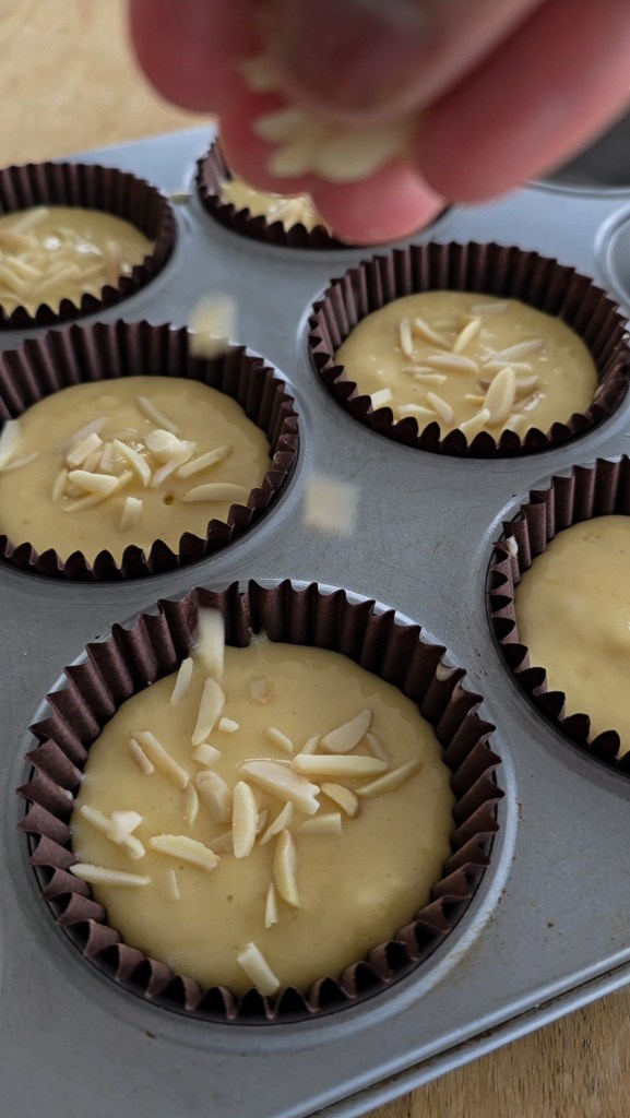 Muffin batter being decorated with almond chips.