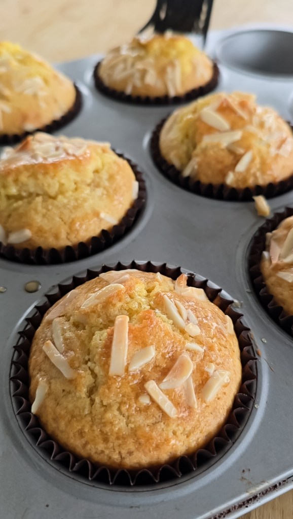 Pan of freshly baked almond croissant muffins out of the oven being glazed.