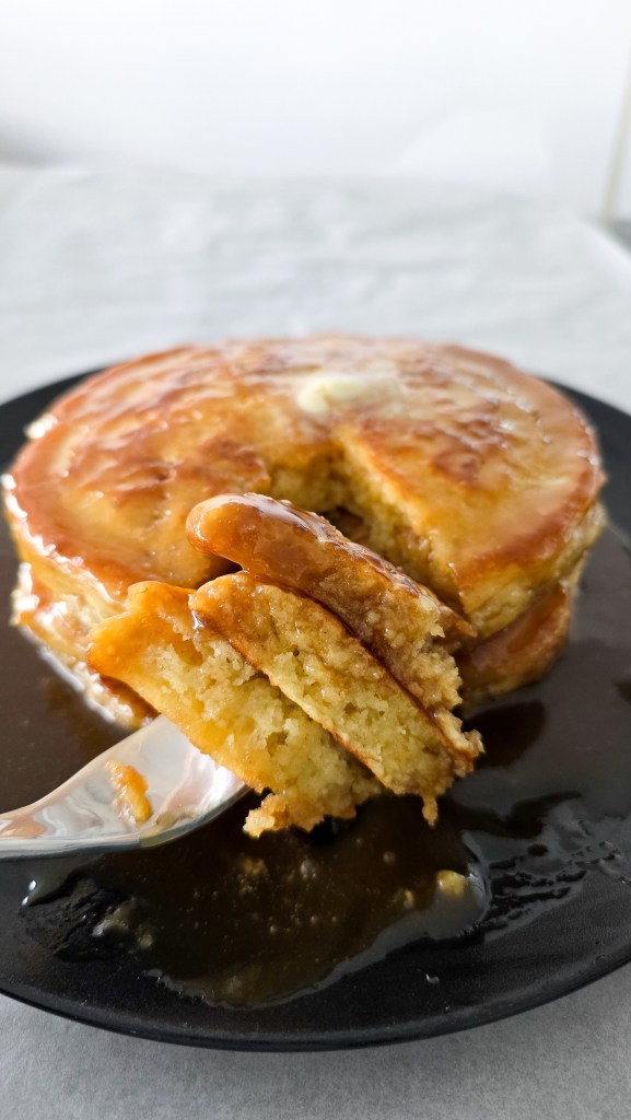 cutting into a stack of buttermilk pancakes with syrup