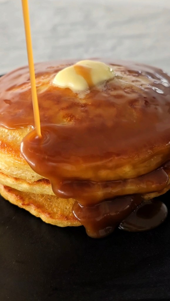 Butterscotch maple syrup being poured on a stack of buttermilk pancakes