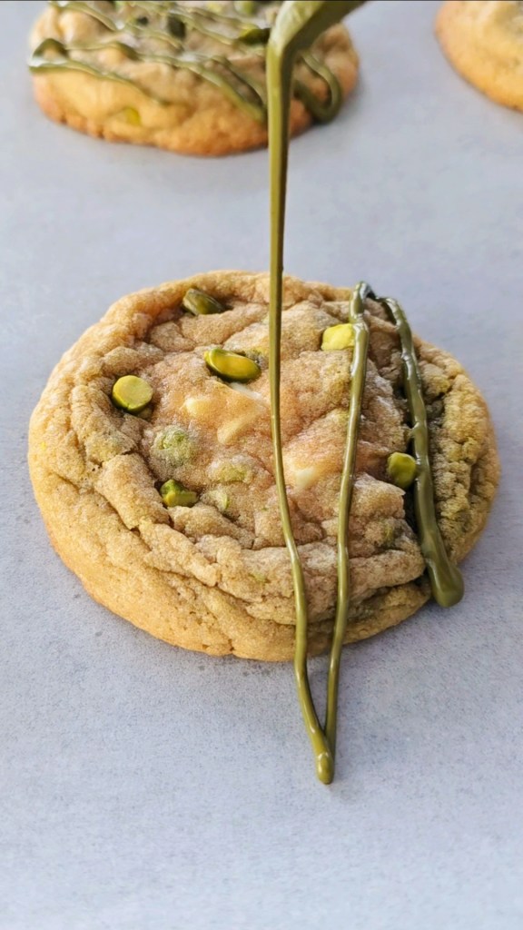 Pistachio drizzle falling on a white chocolate chip cookie